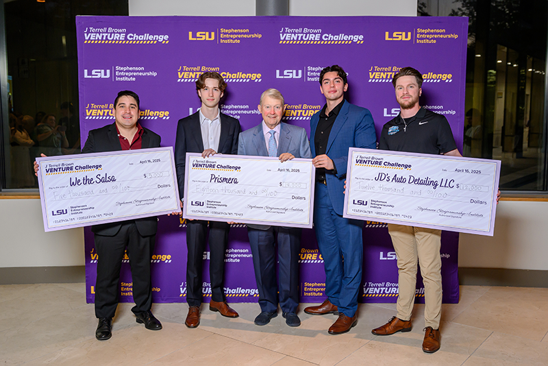 Three teams for LSU students hold large cardboard checks displaying the money they just one in an entrepreneurship pitch competition.