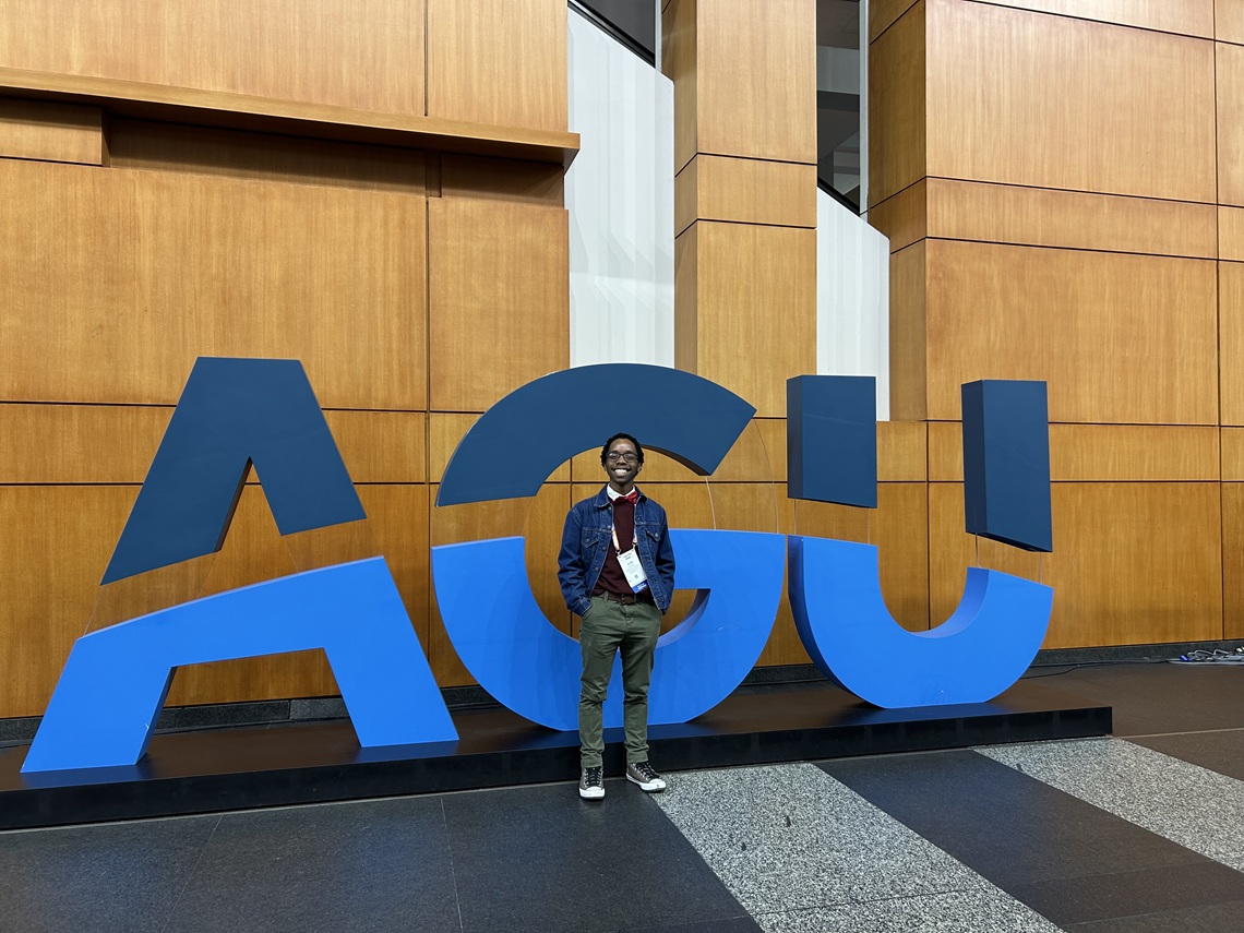 Student posing in front of a sign at a conference